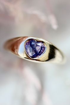 a heart shaped tan and gold ring with a purple stone in the center on a white background