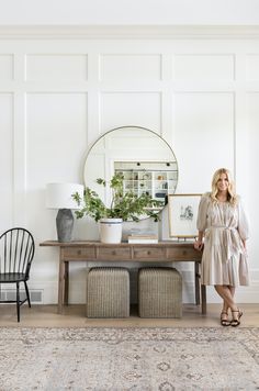 a woman standing in front of a table with plants on it and a mirror behind her