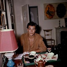 a man sitting at a table in front of a lamp with coffee cups on it