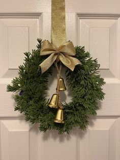 a christmas wreath hanging on the front door with two bells attached to it and a gold bow