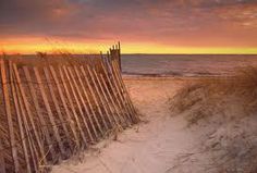 a path leading to the beach with grass and sand on either side, at sunset