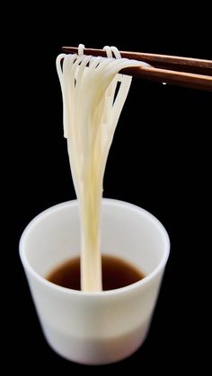 chopsticks are being lifted from a white bowl filled with soup and broth