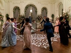 a group of people in formal dress dancing on a wooden floor with floral decorations and chandeliers