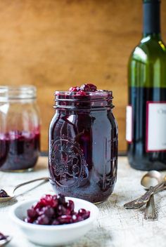 two jars filled with cranberry sauce next to spoons and bottles of wine