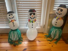 three snowmen with hats and scarfs on standing next to each other in front of a window