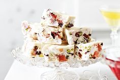 a glass platter filled with fruity treats next to a wine glass and two glasses