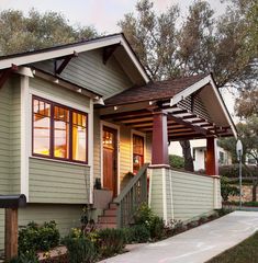 a small house with red trim on the front door and porch, next to a sidewalk