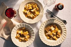 three plates of food on a table with wine and utensils next to it