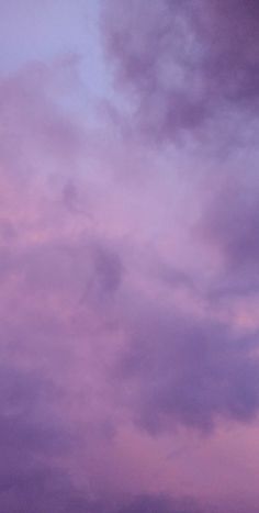 an airplane is flying in the sky with purple and blue clouds behind it on a cloudy day