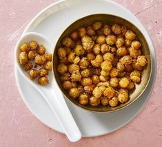 a white plate topped with a bowl filled with fried food next to a spoon on top of a pink surface