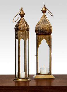 two brass lanterns sitting on top of a wooden table next to a lit candle holder