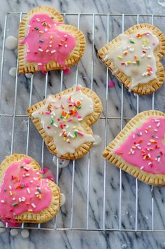 four cookies with pink icing and sprinkles on a cooling rack