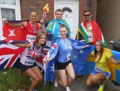 a group of people standing next to each other in front of a house holding flags