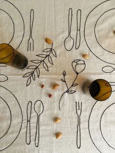 the table cloth has been embroidered onto it with leaves and spoons, along with two empty wine bottles