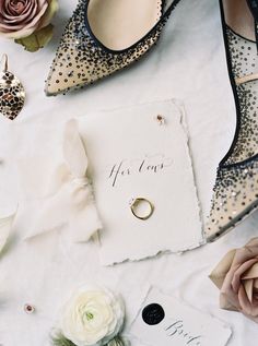 wedding shoes and rings on a white tablecloth with flowers, cards and other items