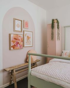 a bedroom with pink walls and pictures on the wall above the bed, along with a bench