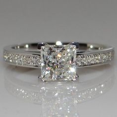 a white gold ring with a princess cut diamond and pave set diamonds on the sides