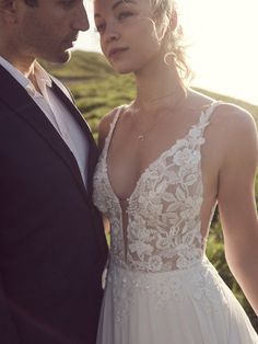 a man and woman standing next to each other in front of a grassy field at sunset