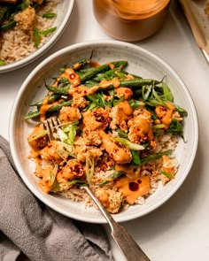 a white plate topped with chicken and veggies covered in sauce next to rice