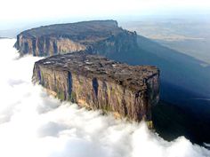 an aerial view of some mountains in the sky with clouds around them and below it