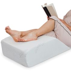 a woman laying on top of a white pillow reading a book while wearing pink pajamas