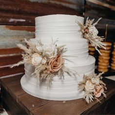 a three tiered white cake with flowers on the top and feathers on the bottom