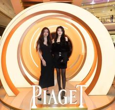 two beautiful women standing next to each other in front of a sign that says piaget