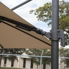 an umbrella is attached to the side of a pole near a fence with trees in the background