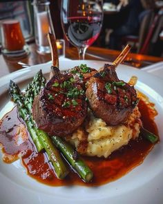 a white plate topped with meat and potatoes covered in gravy next to asparagus