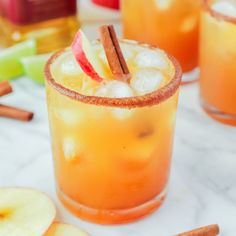 an apple cider cocktail garnished with cinnamon sticks and apples on the side