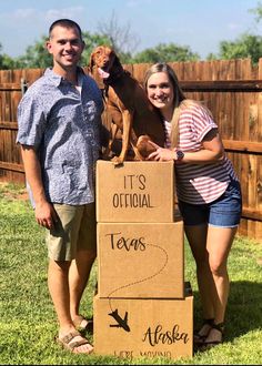 a man and woman standing next to a cardboard box with a dog on it's back