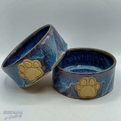 two blue ceramic bowls with gold paw prints on them, one is empty and the other has an animal's paw painted on it