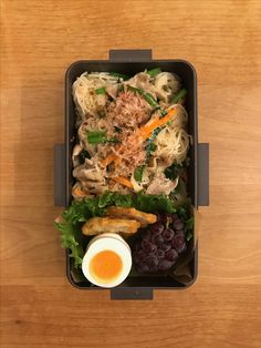 a bento box filled with noodles, meat and veggies next to an egg