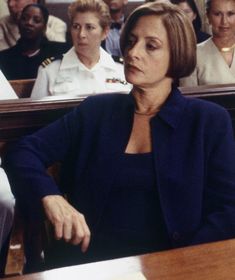 a woman sitting at a table with other people in the audience behind her looking off into the distance