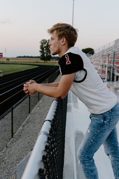 a young man leaning against a fence on the side of a football field at sunset