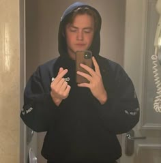 a person taking a selfie in the mirror with a cell phone and wearing a hoodie