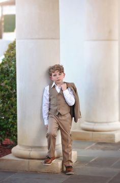 a young boy in a suit leaning against a pillar