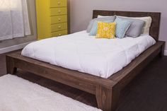 a bed with white sheets and pillows in a bedroom next to a yellow chest of drawers