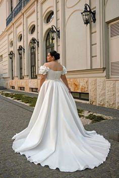 a woman in a white wedding dress is standing on the side walk near a building