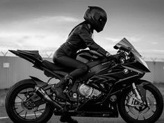 a woman in black riding on the back of a motorcycle