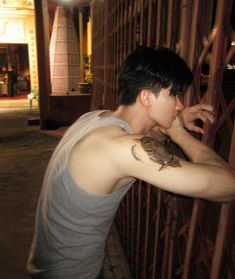 a young man with a tattoo on his arm leaning against a fence in front of a building