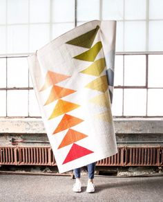 a woman holding up a colorful quilt in an industrial building