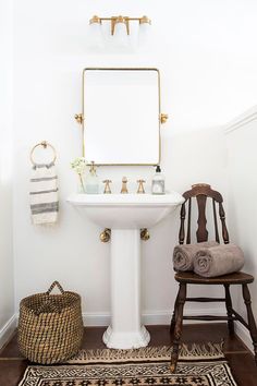 a white pedestal sink sitting next to a wooden chair in a bathroom under a mirror