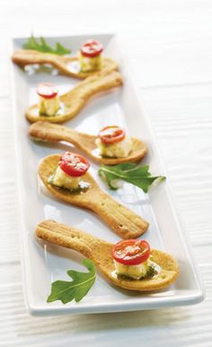 several small appetizers are arranged on a white platter with green leafy garnishes