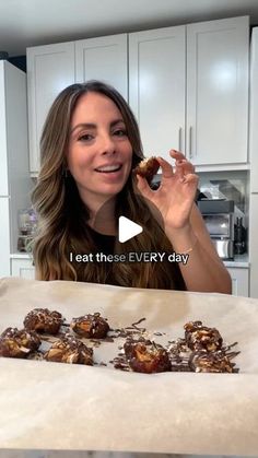 a woman is eating chocolate covered donuts on a table in front of white cabinets