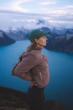 a woman standing on top of a mountain next to a blue lake with mountains in the background