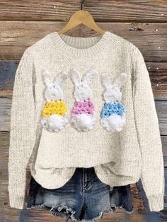 a sweater with three crocheted rabbits on it, hanging up against a wooden wall