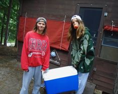 two young women standing in front of a house with a cooler on the ground next to them