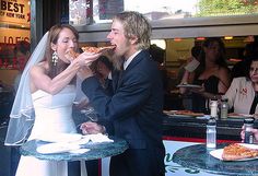 a bride and groom eating pizza in front of a restaurant