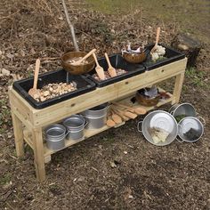 a wooden table with pots and pans on it in the grass next to trees